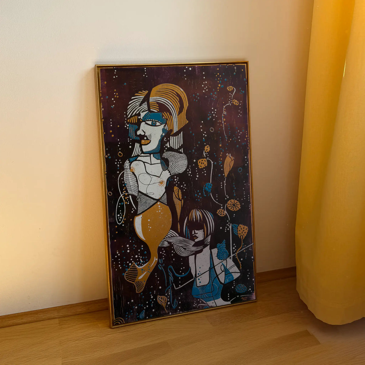 The linocut Underwater Love, framed in a gold shadow-joint frame, stands on a wooden floor and is leaning against the beige wall. It depicts two stylized figures among aquatic plants and bubbles.