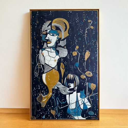 The linocut Underwater Love, framed in a gold shadowbox frame, stands on a wooden floor and is leaning against the beige wall. It depicts two stylized figures among aquatic plants and bubbles.