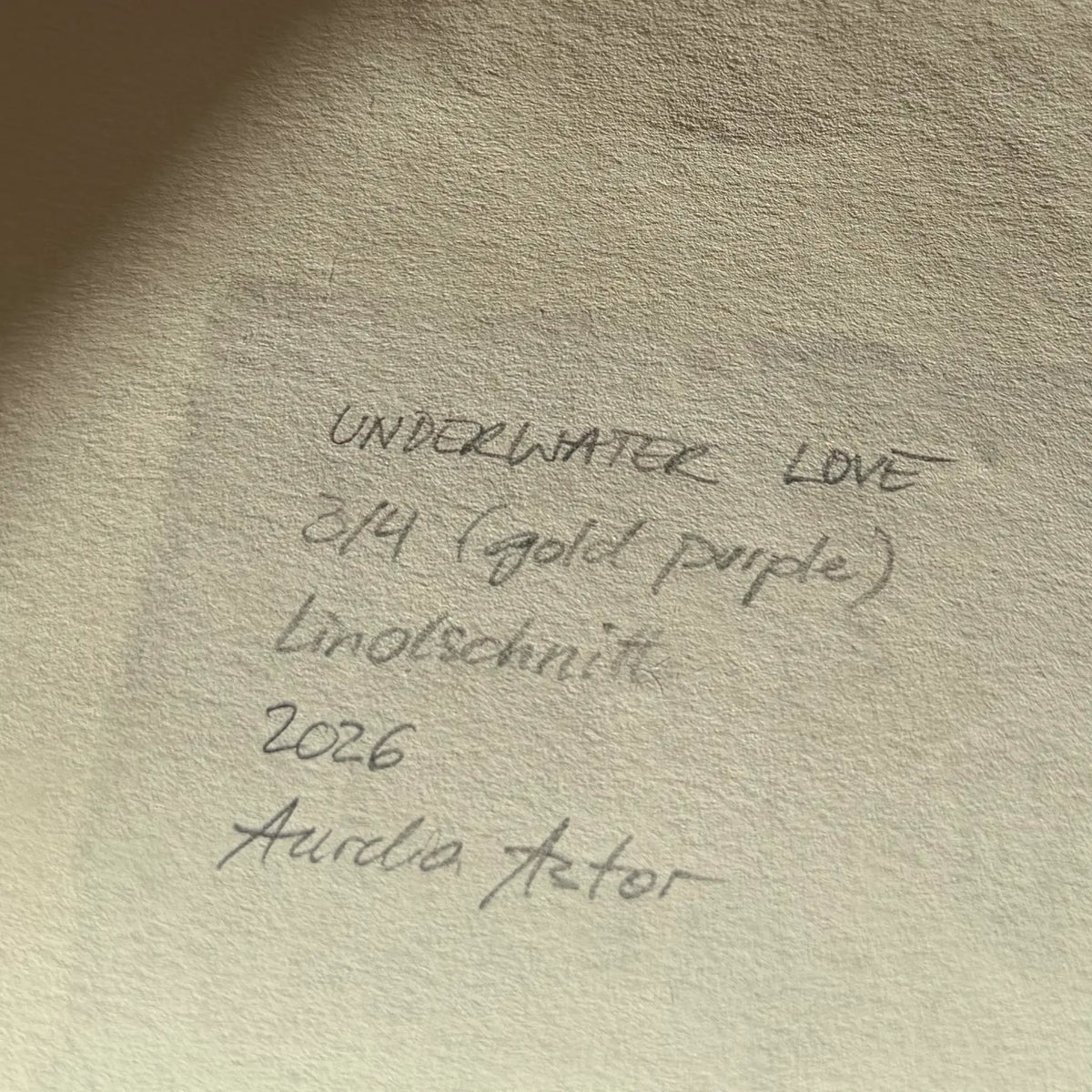 Information about the artwork and the signature, written in pencil on the back of the linocut: Underwater Love, 3/4 (gold purple), linocut, 2026, Aurelia Astor